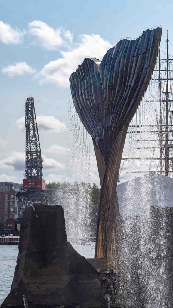 Achim Kühnin "Harmonia"-suihkulähde Turun Aurajoessa, taustalla purjelaivojen mastot ja satamanosturi kirkkaan taivaan alla.