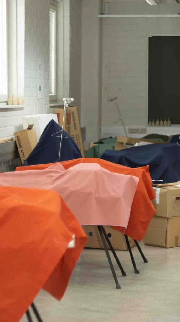 Tyhjä koneneulonnan luokkahuone EKAMissa Haminassa, peitettyjä koneita ja pahvilaatikoita. Kuva symboloi koulutuksen päättymistä ja aikakauden loppua.