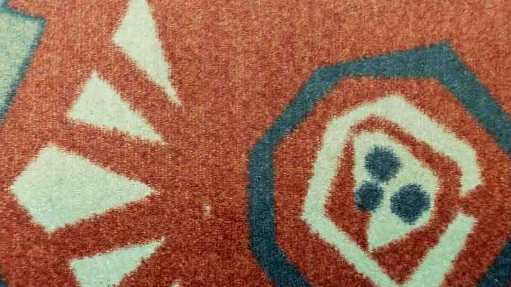 Lähikuva Imatran Valtionhotellin vanhasta matosta, jossa on oranssin ja turkoosin sävyinen geometrinen kuvio.