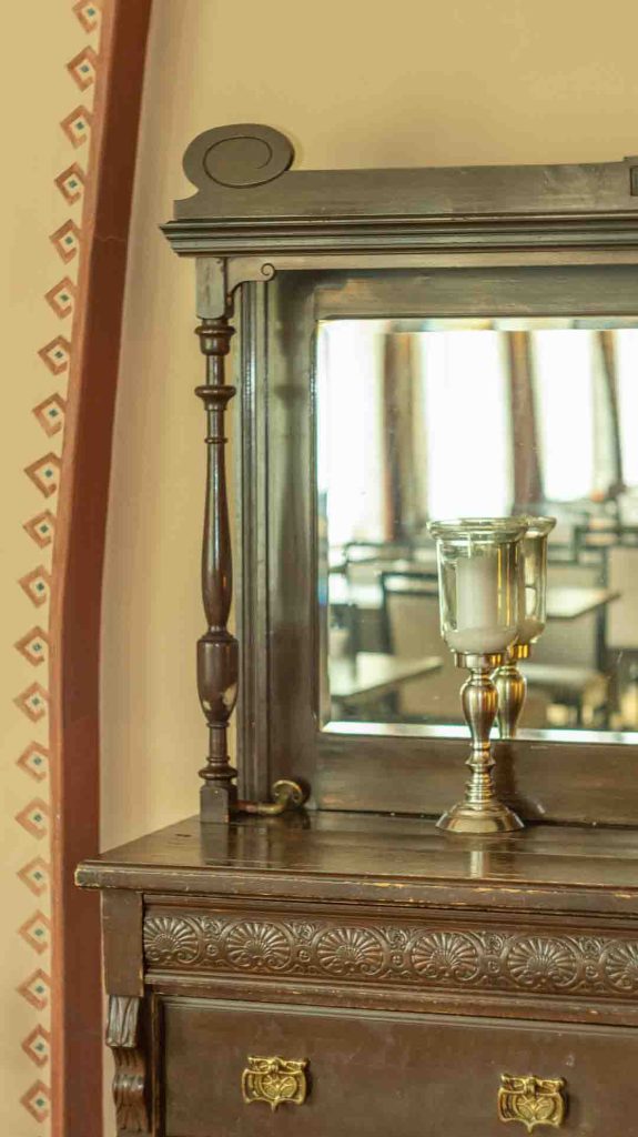 Imatran Valtionhotellin vanha puinen lipasto peileineen ja kynttilänjalalla, heijastaen hotellin sisätiloja.