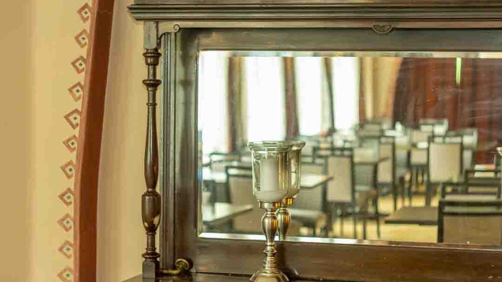 Lähikuva Imatran Valtionhotellin vanhasta puisesta lipastosta, korostuen sen koristeelliset kaiverrukset ja peiliheijastus.