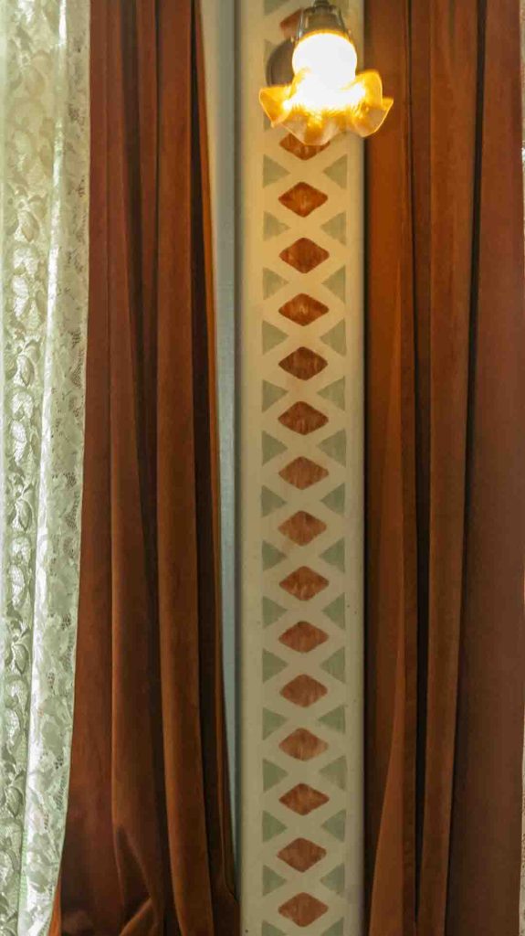 Lähikuva Imatran Valtionhotellin seinäkuviosta, ruskeasta verhosta ja pitsiverhosta.