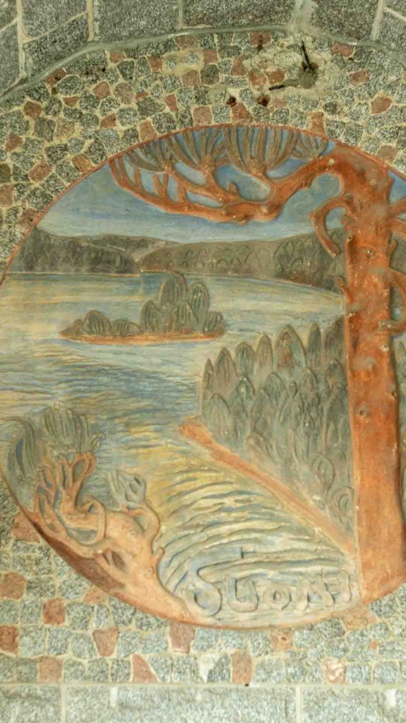 Imatran Valtionhotellin ulkoseinän pyöreä reliefi, joka esittää tyyliteltyä maisemaa puineen ja vedenvirtoineen.