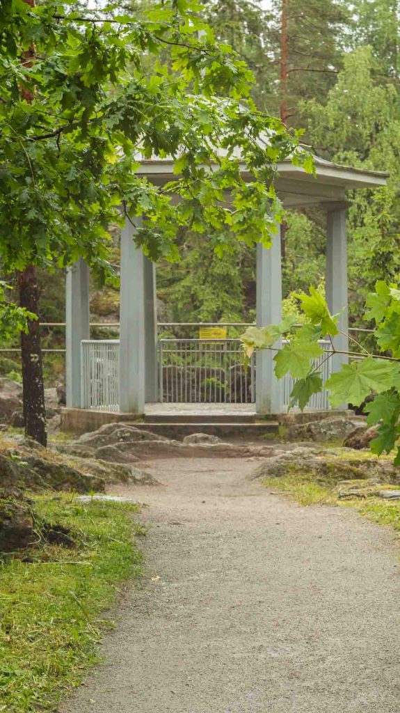 Valkoinen, pylväiden kannattelema paviljonki Imatran luonnon keskellä, jonne johtaa polku. Kuva symboloi rauhallista ja inspiroivaa vetäytymispaikkaa.