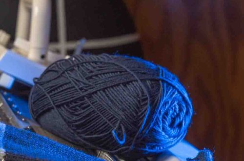 Lähikuva tummansinisestä villalangasta ja vaaleanraidoitetusta neuloksesta Brother koneneulekoneen pedillä. Kuva korostaa langan laatua ja neuleen tekstuuria.