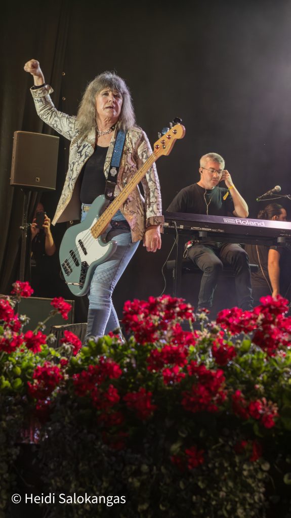  Suzi Quatro nostaa kätensä ilmaan soittaessaan bassoa lavalla.