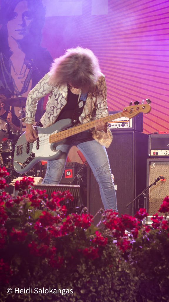 Suzi Quatro soittaa bassoa lavalla, hiukset peittävät kasvot.