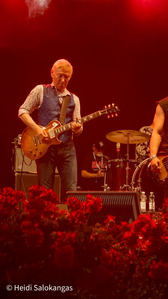 Mies soittaa sähkökitaraa lavalla punaisen valaistuksen alla.