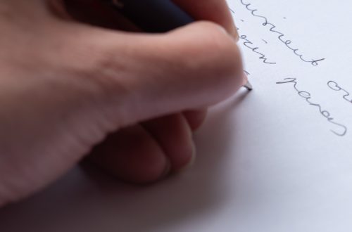 Käsi kirjoittaa mustekynällä valkoiselle paperille.