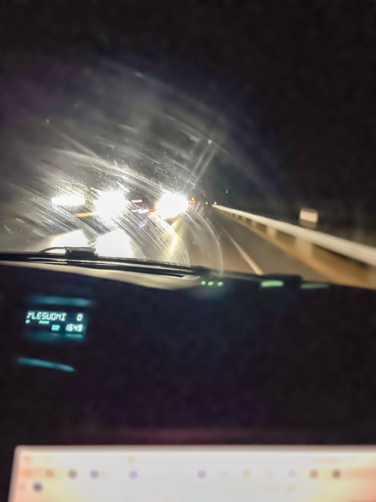 Pimeä tie ja vastaantulevien autojen valot auton tuulilasin läpi kuvattuna.