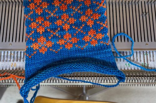 Kirjoneule neulekoneella sähkönsinisenä ja oranssina, osa modernia Louhiatar-neulemallistoa.