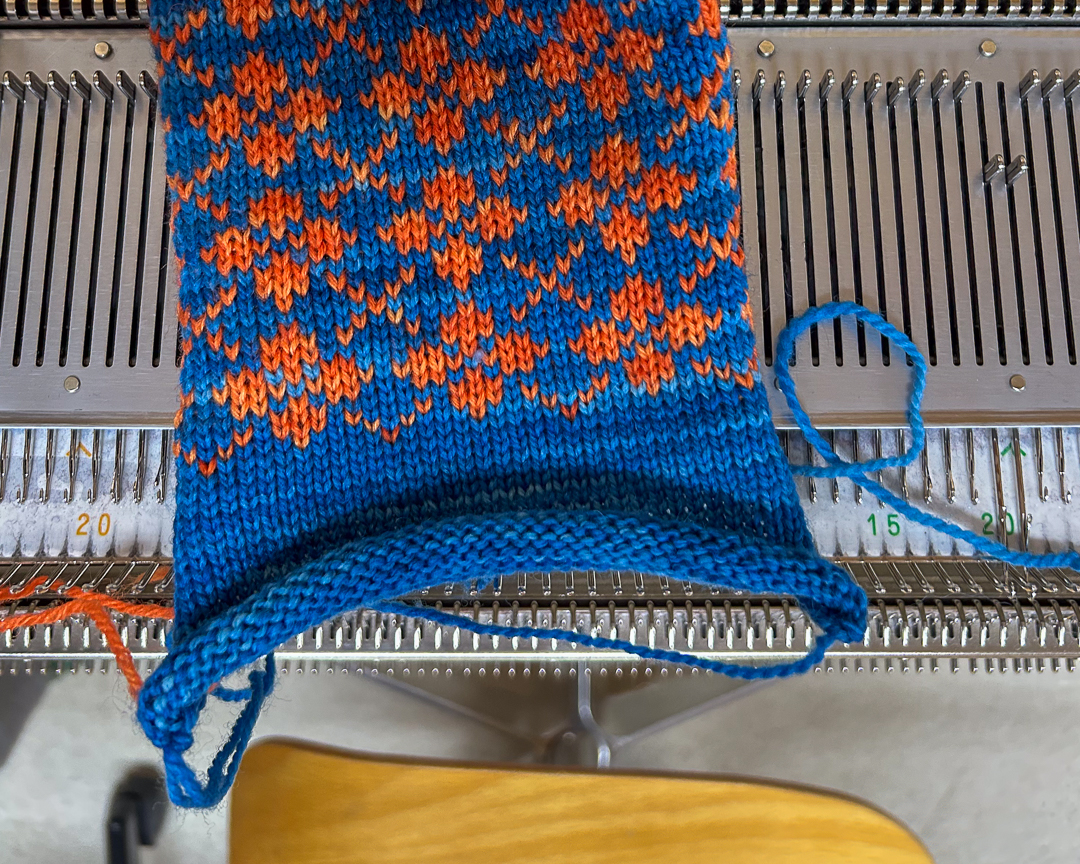 Kirjoneule neulekoneella sähkönsinisenä ja oranssina, osa modernia Louhiatar-neulemallistoa.