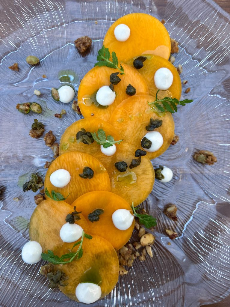 Kurpitsacarpaccio viipaloitu kurpitsa siemengranolalla, tahinikreemipisteillä ja kapriksilla KasvisPro‑menun alkuruokana.