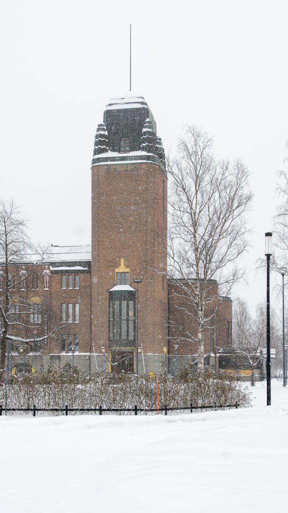 Joensuun kaupungintalo lumisateessa talvella, punatiilinen rakennus ja torni