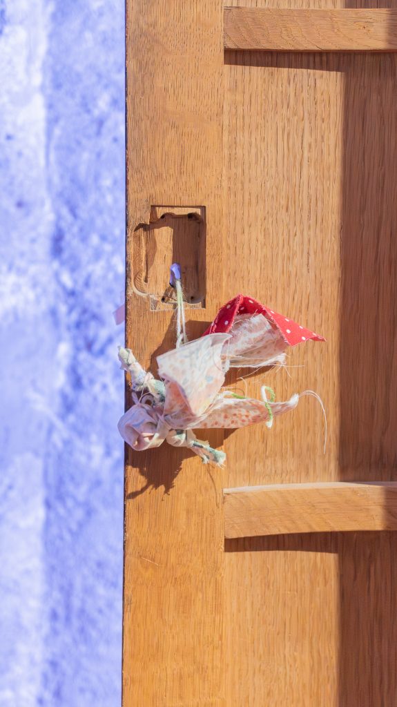 Pienikokoinen karjalainen suojelusnukke ripustettuna puiseen oveen museon näyttelyssä