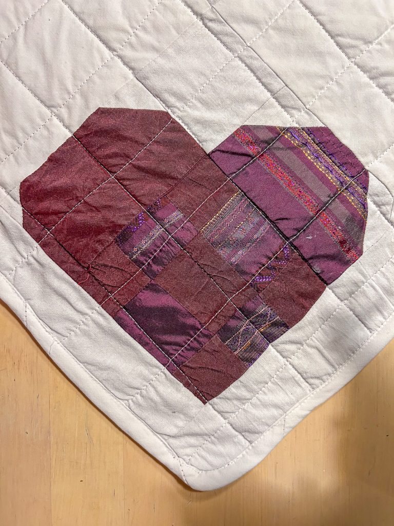 Tilkkutyö sydän silkkitilkuista valkoisella tikatulla kankaalla, kierrätyskankaista ommeltu ystävänpäivän pöytäliina.