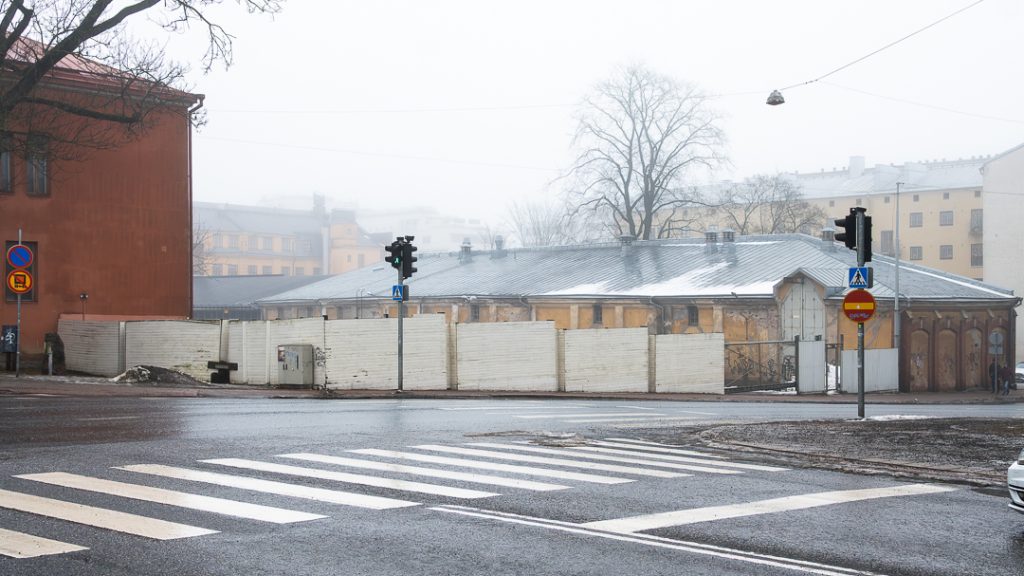 Sumuinen risteys Turussa: suojatie, liikennevalot ja aidatun vanhan rakennuksen siluetti harmaassa aamussa.