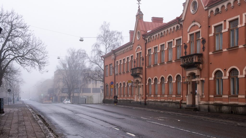 Sumuinen katunäkymä Turussa: punaruskea historiallinen rakennus, märkä ajorata ja harmaaseen katoava katu talviaamuna.