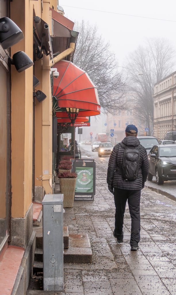 Sumuinen katu Turussa: yksittäinen kävelijä liikkuu hiljaisella tiellä puutalon ja pysäköityjen autojen ohi.