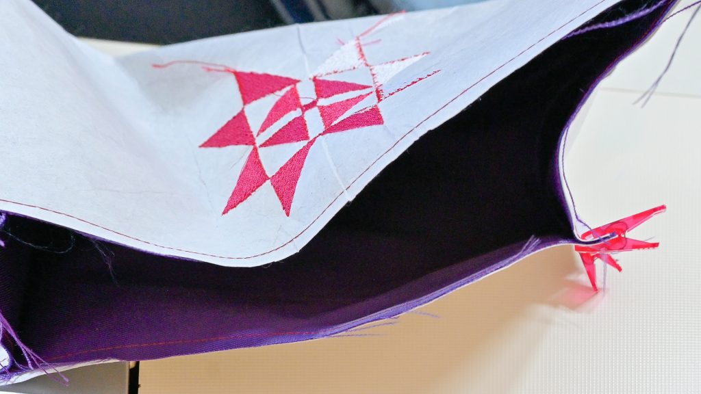 Valkoinen Cut-A-Way-tukikangas violetin päälliskankaan nurjalla puolella kesken kangaslaatikon ompelun.