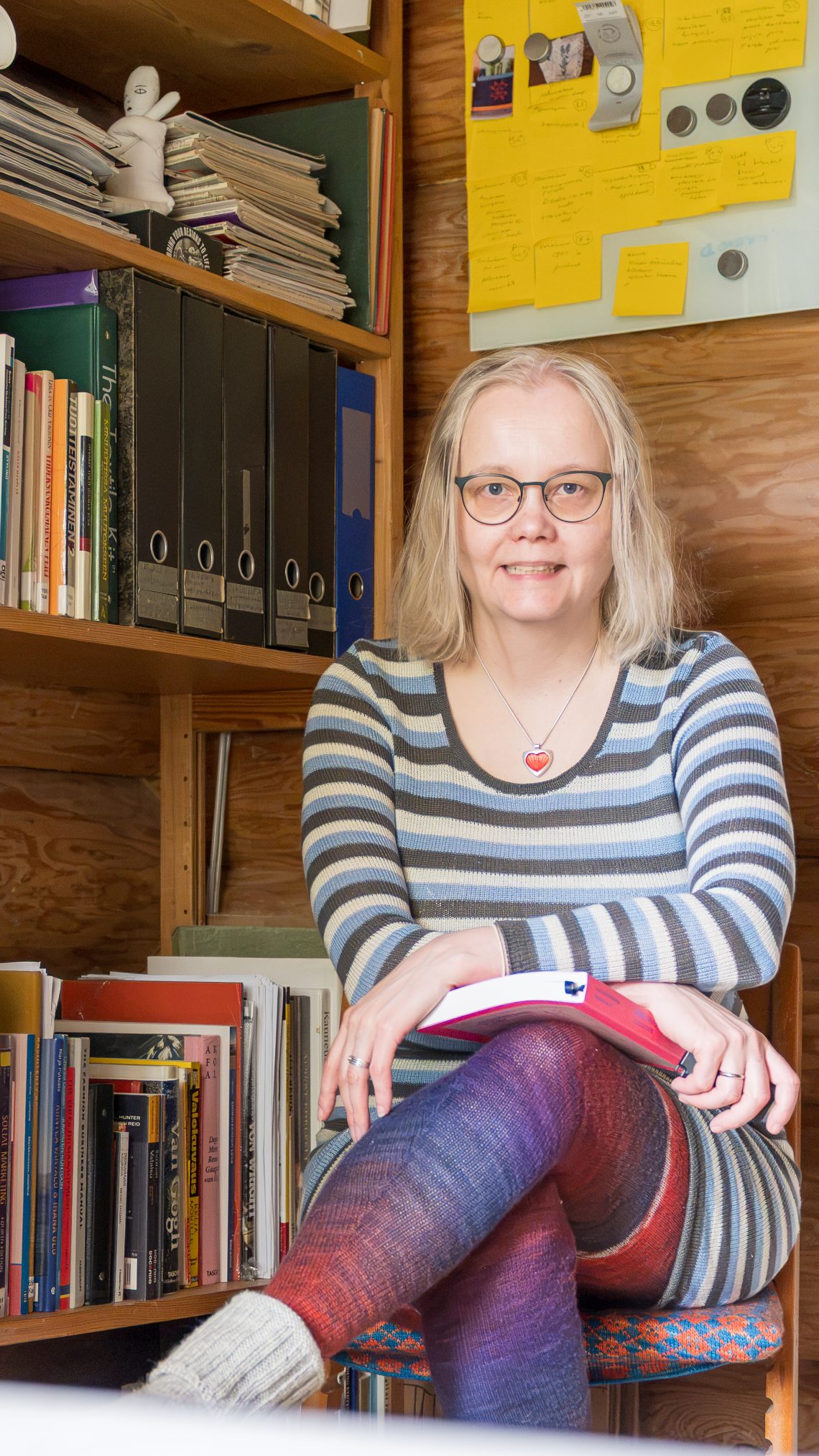 Heidi Salokangas istuu työhuoneessa raidallinen neulemekko yllään.