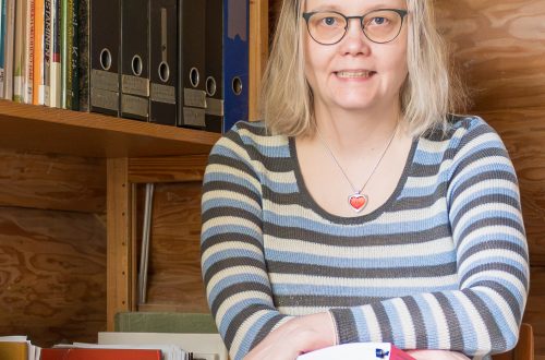 Heidi Salokangas istuu työhuoneessa raidallinen neulemekko yllään.