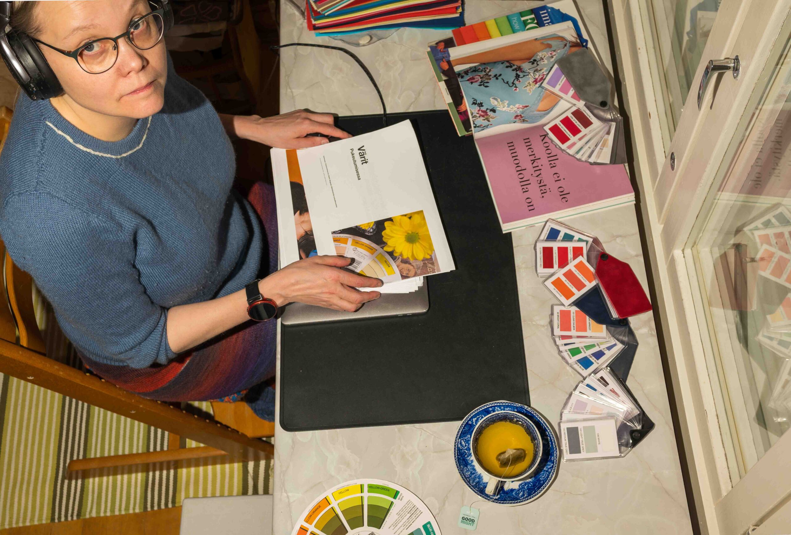 Heidi selaa Värit pukeutumisessa -kirjaa värikorttien ja väriviuhkojen äärellä.